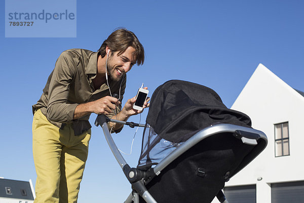Mann zeigt Handy einem Baby im Kinderwagen