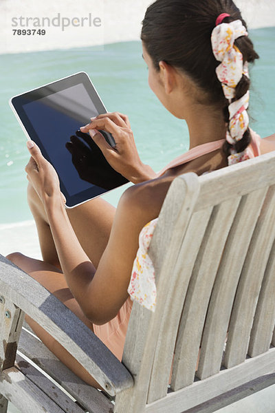 Frau sitzt auf einem Stuhl und benutzt ein digitales Tablett am Strand.