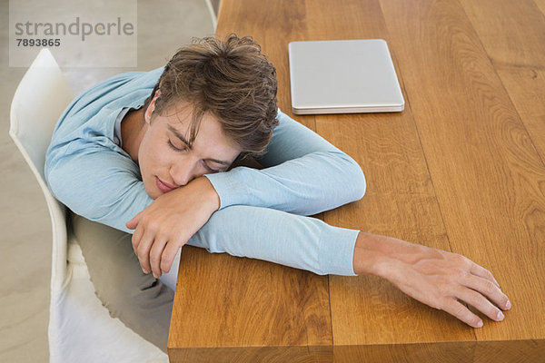 Hochwinkelansicht eines Mannes  der auf einem Tisch mit einem Laptop schläft.