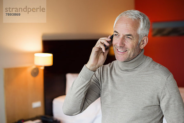 Ein Mann  der auf einem Handy in einem Hotelzimmer spricht.