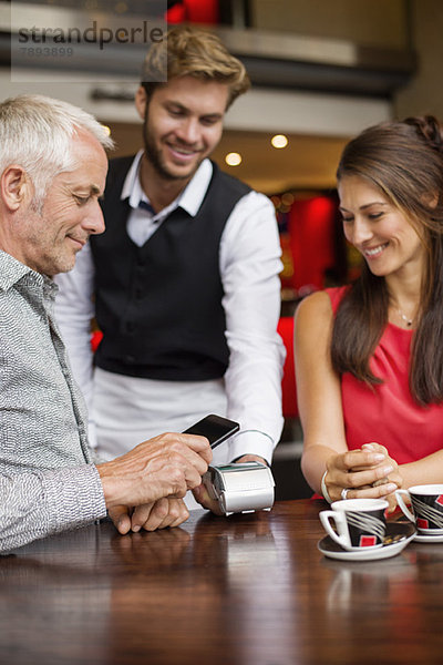 Kellner zeigt einem Paar auf einem Tisch in einem Restaurant ein Kreditkartenlesegerät.