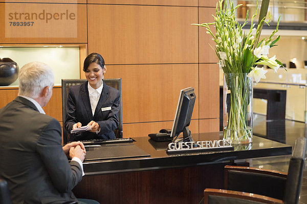 Rezeptionistin  die einem Geschäftsmann an der Hotelrezeption Broschüren überreicht.