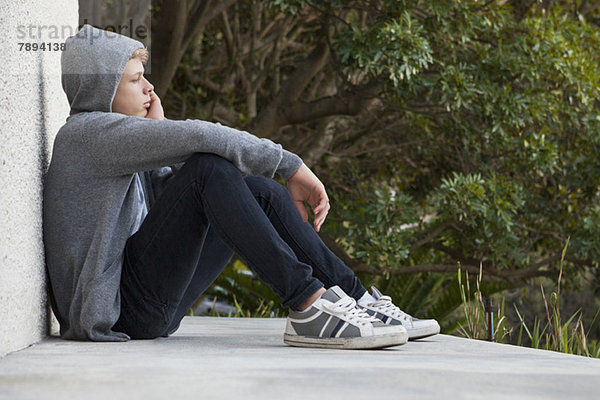Teenager-Junge  der sich an eine Wand lehnt und denkt.