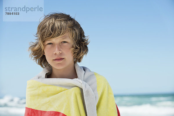 Porträt eines in ein Handtuch gewickelten Jungen am Strand