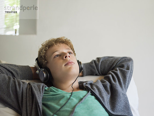 Teenager-Junge auf dem Bett liegend und Musik hörend