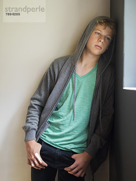 Teenager-Junge  der sich an eine Wand lehnt und denkt.