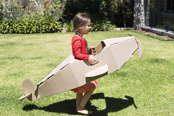 Mädchen beim Spielen mit einem Flugzeug aus Pappe im Rasen