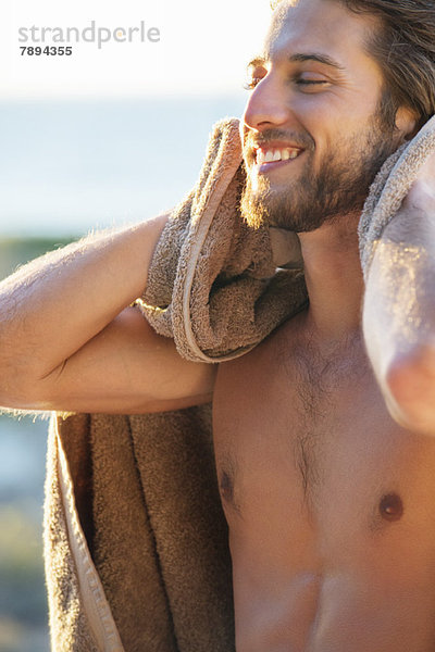 Glücklicher Mann wischt sich mit einem Handtuch am Strand ab