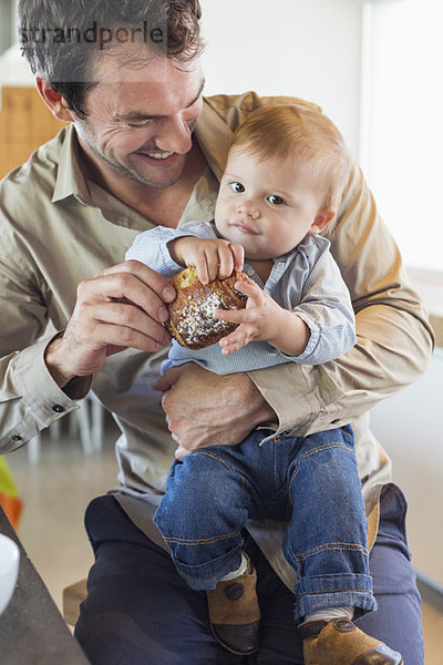 Mann füttert seinen Sohn an einer Küchentheke mit Brot.