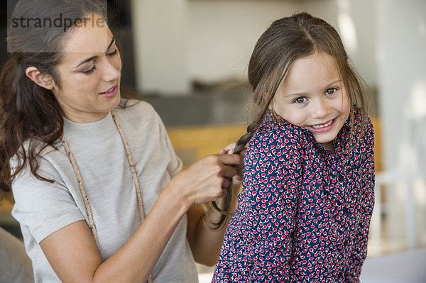 Lächelnde Frau  die das Haar ihrer Tochter flechtet.