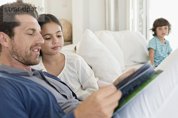 Mann beim Lesen einer Zeitschrift mit seiner Tochter und seinem Sohn im Hintergrund