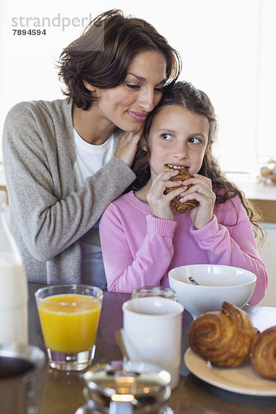 Mädchen frühstückt neben ihrer Mutter an der Küchentheke