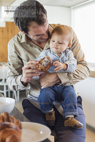 Mann füttert seinen Sohn an einer Küchentheke mit Brot.