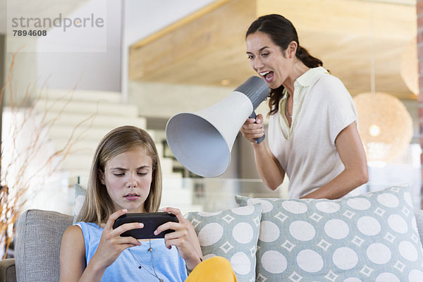 Frau schreit durch ein Megaphon seine Tochter an  weil sie Videospiel spielt.