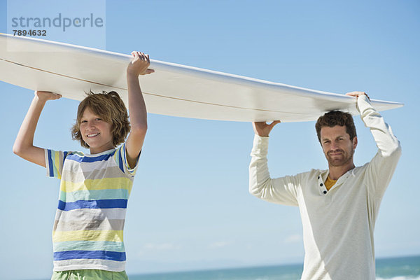 Mann und Sohn mit Surfbrett am Strand