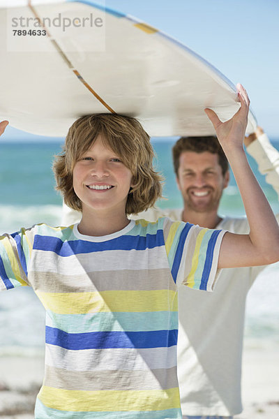 Mann und Sohn mit Surfbrett am Strand