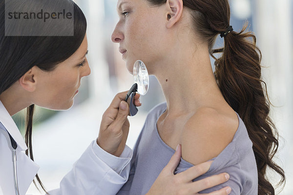 Dermatologe untersucht Frauenhaut mit Lupe