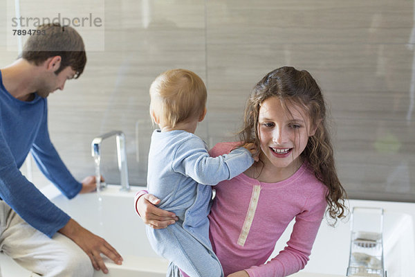 Mädchen lächelt mit ihrem Bruder und ihrem Vater auf einem Wannenrand im Bad.