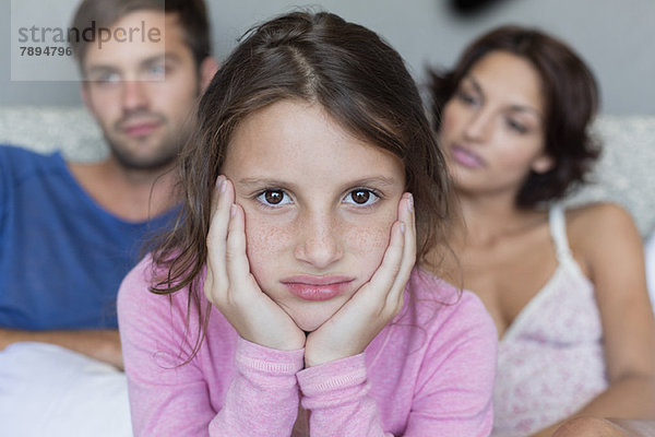 Porträt eines Mädchens  das mit seinen Eltern im Hintergrund verärgert aussieht.