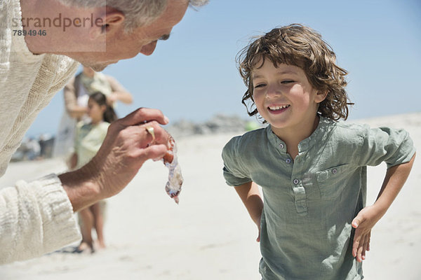 Mann zeigt seinem Enkel am Strand eine Qualle