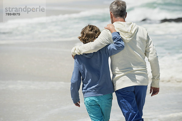 Mann  der mit seinem Enkel am Strand spazieren geht.