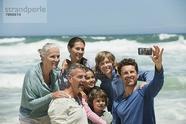 Glückliche Mehrgenerationen-Familie beim Selbstporträt mit dem Handy am Strand