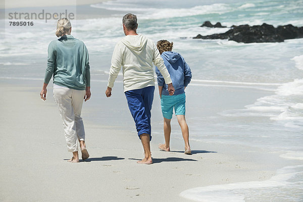 Junge  der mit seinen Großeltern am Strand spazieren geht.