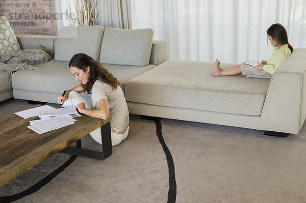 Frau  die mit ihrer Tochter Papierkram erledigt  indem sie zu Hause ein digitales Tablett benutzt.