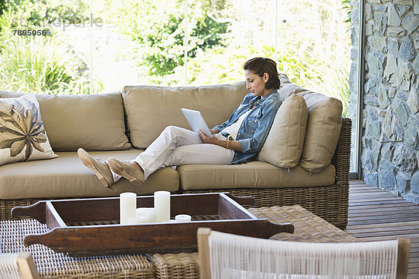 Frau auf einer Couch liegend und mit einem digitalen Tablett