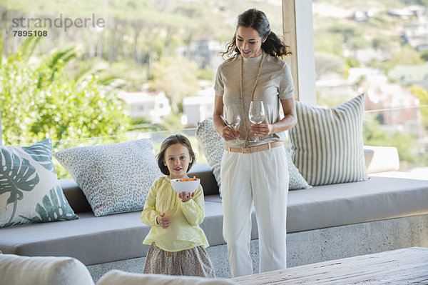 Mädchen hält eine Schale mit Snacks neben ihrer Mutter und hält eine Stielgläser zu Hause.