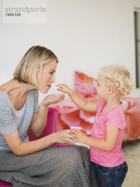 Mädchen füttert Joghurt an ihre Mutter