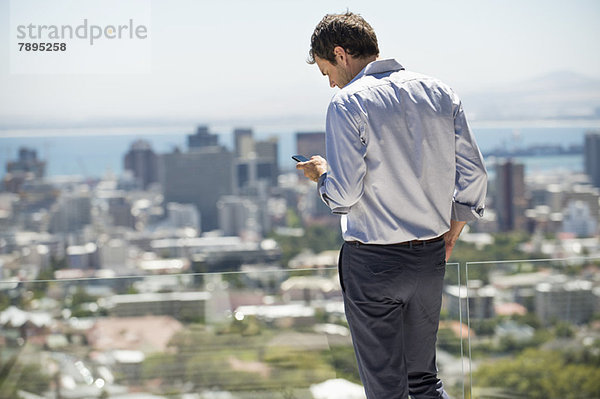 Auf der Terrasse stehender Mann mit dem Handy
