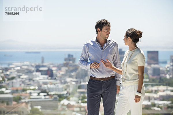 Paar diskutiert auf einer Terrasse mit Stadt im Hintergrund