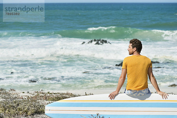 Mann auf einem Surfbrett am Strand sitzend