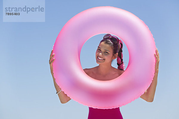 Schöne Frau  die durch einen aufblasbaren Ring am Strand schaut.