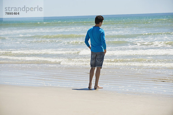 Mann steht am Strand und schaut auf das Meer.