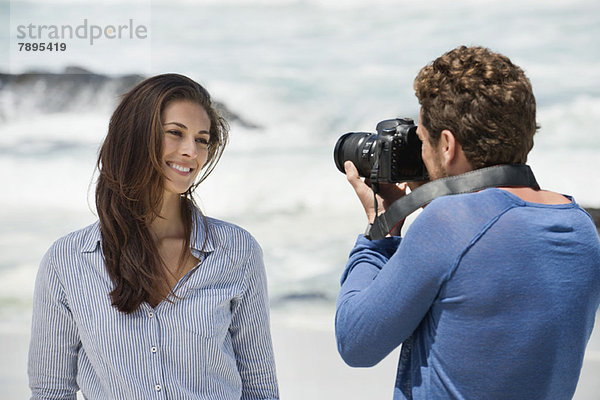 Mann beim Fotografieren seiner Frau mit einer Kamera am Strand