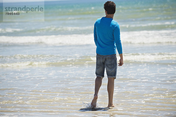 Mann steht am Strand und schaut auf das Meer.