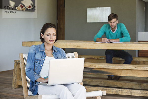 Frau mit Laptop und ihrem Mann im Hintergrund