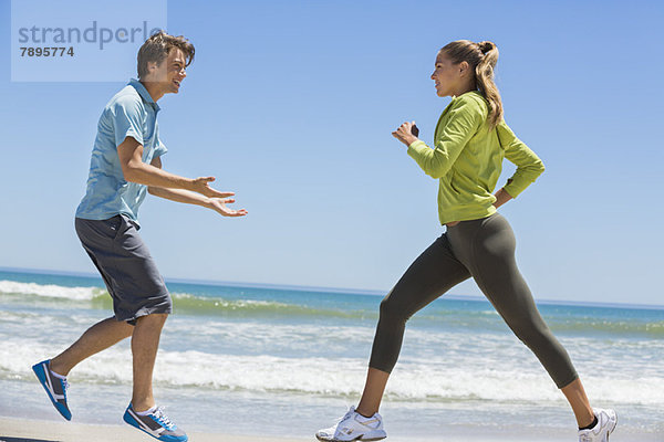 Frau beim Joggen am Strand mit ihrem Trainer
