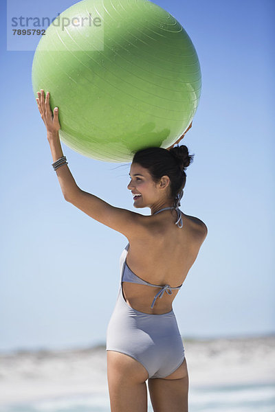 Schöne Frau mit einem Fitnessball am Strand