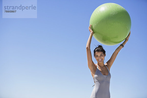 Schöne Frau mit einem Fitnessball am Strand