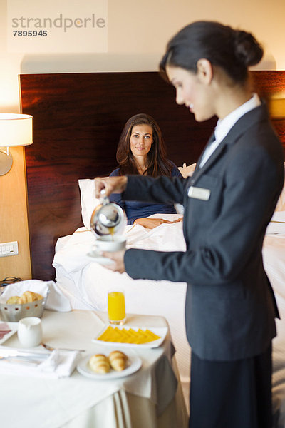 Kellnerin  die einer Frau im Hotelzimmer Tee serviert.