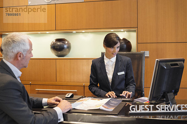 Rezeptionist bei der Arbeit an einem Desktop-PC mit einem Geschäftsmann an der Hotelrezeption