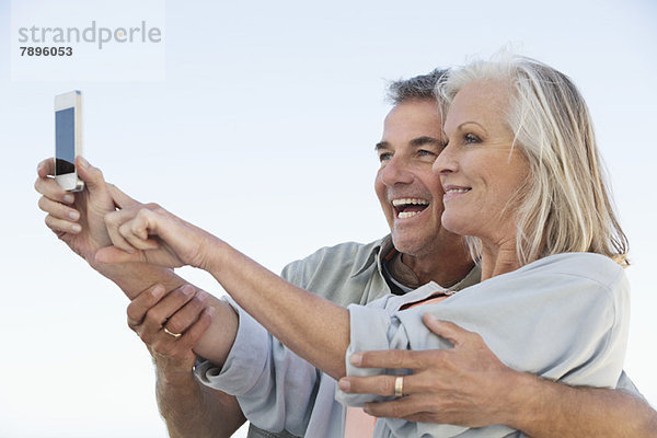 Ein Paar macht ein Foto von sich mit einem Handy am Strand.