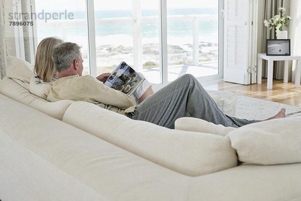 Ein Paar sitzt auf einer Couch und liest eine Zeitschrift.
