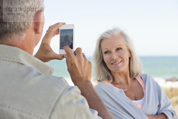 Mann fotografiert seine Frau mit einem Handy am Strand