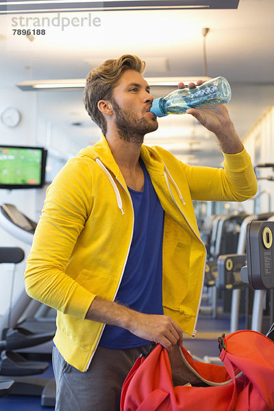 Mann trinkt Wasser aus einer Flasche im Fitnessstudio