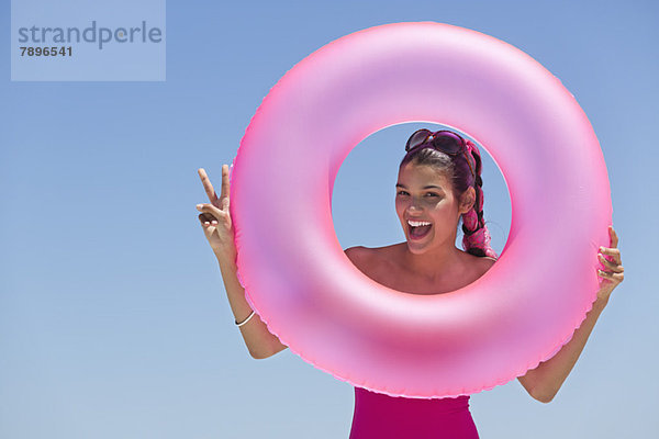 Schöne Frau  die durch einen aufblasbaren Ring am Strand schaut.