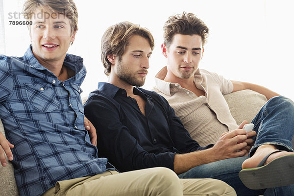Drei männliche Freunde sitzen zusammen auf einer Couch.